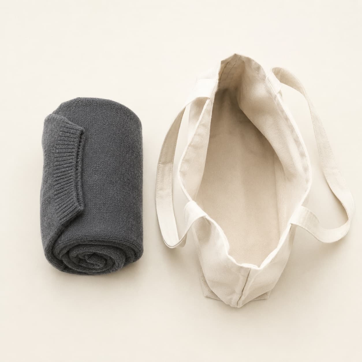 A tightly rolled wool sweater resting beside the open mouth of a canvas tote bag
